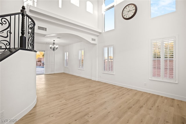 foyer entrance featuring a towering ceiling, a notable chandelier, and light wood-type flooring