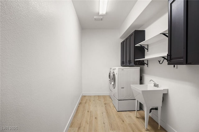 laundry area with light hardwood / wood-style floors, cabinets, and washing machine and clothes dryer