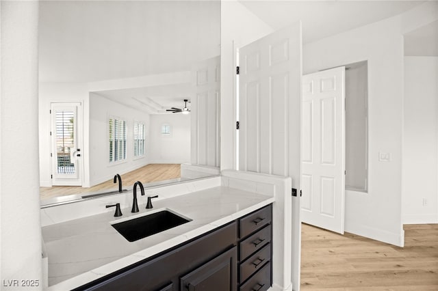 interior space with dark brown cabinetry, light hardwood / wood-style floors, sink, ceiling fan, and light stone counters