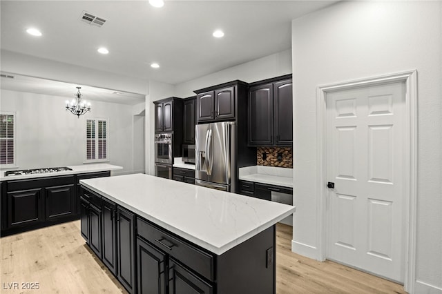 kitchen featuring light hardwood / wood-style floors, stainless steel appliances, backsplash, decorative light fixtures, and a center island