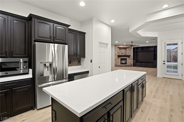 kitchen featuring light hardwood / wood-style floors, a stone fireplace, stainless steel appliances, tasteful backsplash, and a center island