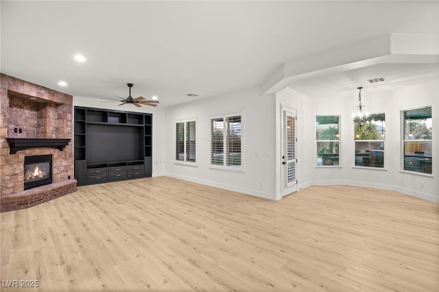 unfurnished living room with built in shelves, a fireplace, ceiling fan with notable chandelier, and light hardwood / wood-style floors