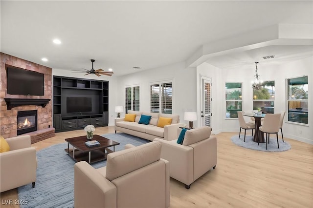 living room with ceiling fan with notable chandelier, built in shelves, light hardwood / wood-style flooring, and a stone fireplace