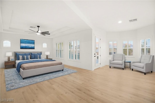 bedroom featuring ceiling fan, multiple windows, a tray ceiling, and light wood-type flooring