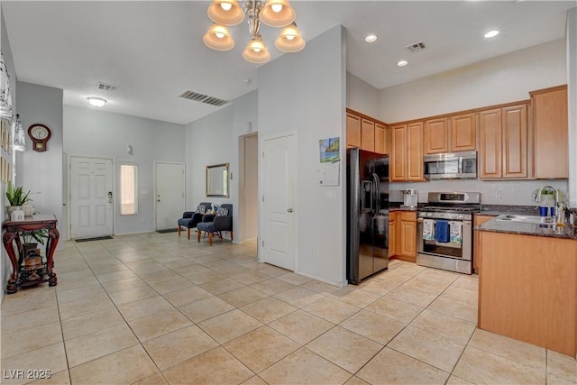 kitchen with a towering ceiling, stainless steel appliances, sink, a chandelier, and light tile patterned flooring