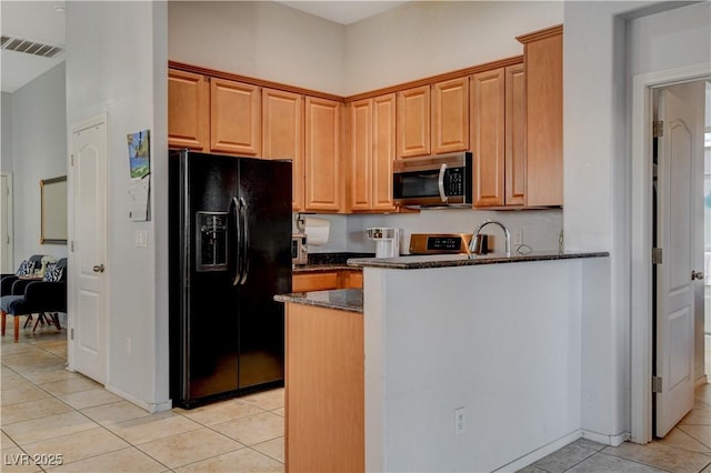 kitchen featuring light tile patterned floors, appliances with stainless steel finishes, and dark stone counters