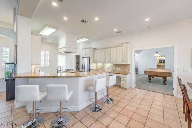 kitchen featuring white cabinets, pool table, stainless steel fridge, kitchen peninsula, and a breakfast bar