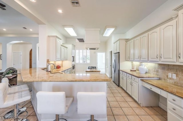 kitchen with appliances with stainless steel finishes, sink, kitchen peninsula, a breakfast bar, and light tile patterned floors