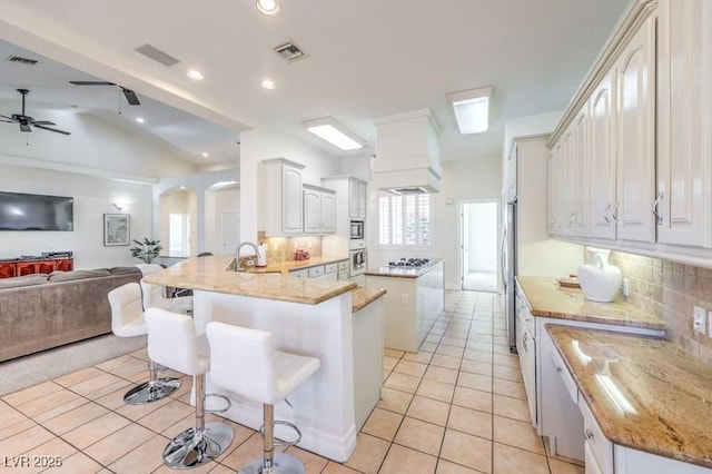 kitchen with light tile patterned floors, kitchen peninsula, decorative backsplash, a breakfast bar, and sink