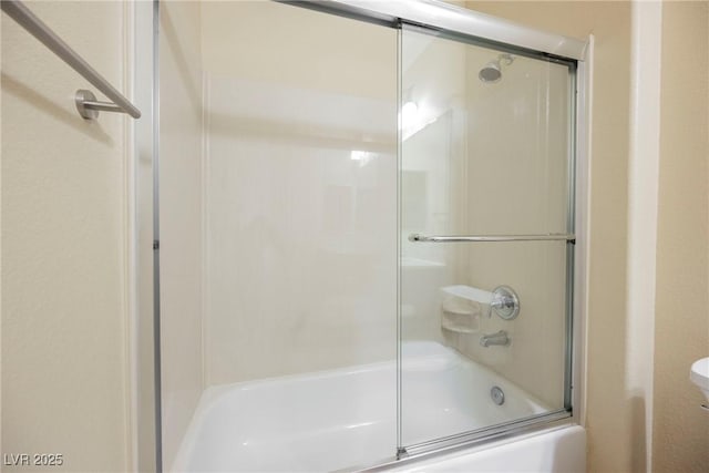 bathroom featuring toilet and bath / shower combo with glass door