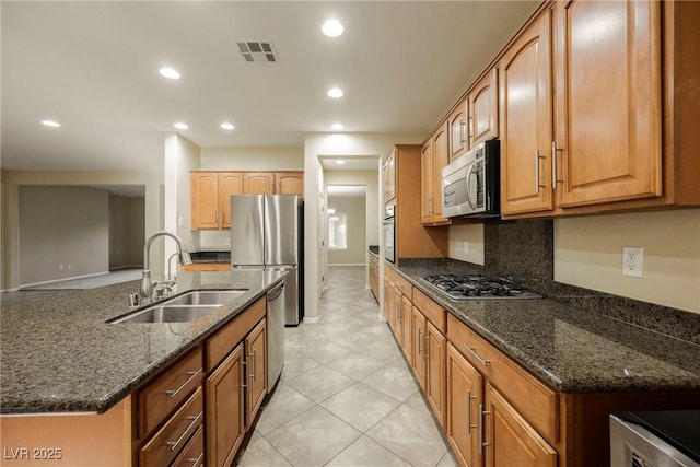 kitchen with stainless steel appliances, sink, a center island with sink, and dark stone countertops