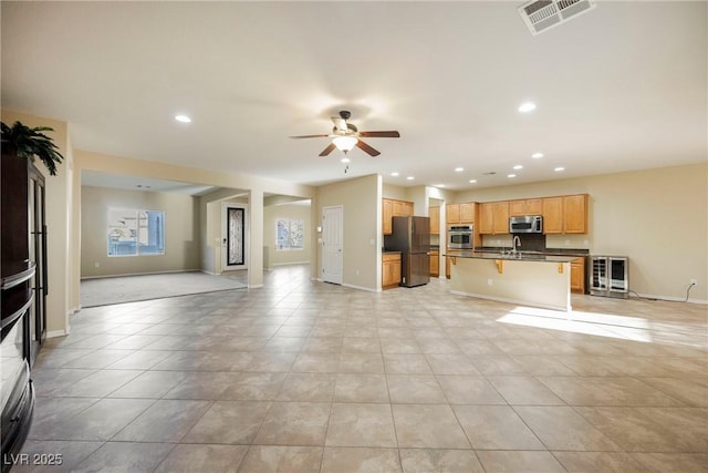 unfurnished living room with ceiling fan, beverage cooler, sink, and light tile patterned floors