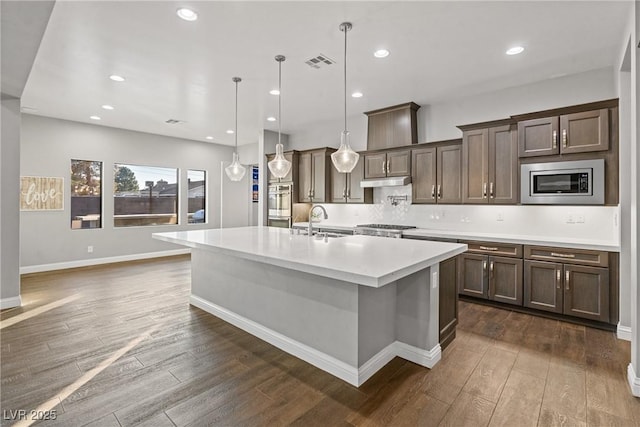 kitchen with pendant lighting, dark brown cabinetry, stainless steel appliances, and a kitchen island with sink