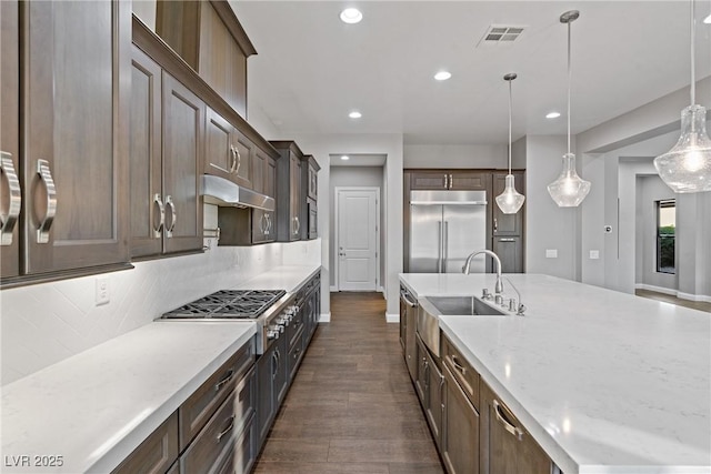 kitchen featuring appliances with stainless steel finishes, pendant lighting, backsplash, and light stone counters