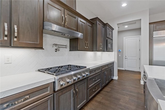 kitchen featuring tasteful backsplash, dark hardwood / wood-style floors, built in appliances, and dark brown cabinets