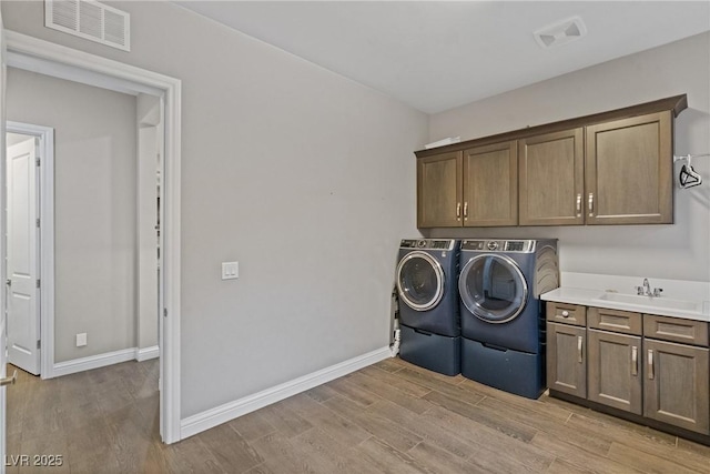 clothes washing area featuring cabinets, sink, light hardwood / wood-style flooring, and washer and dryer