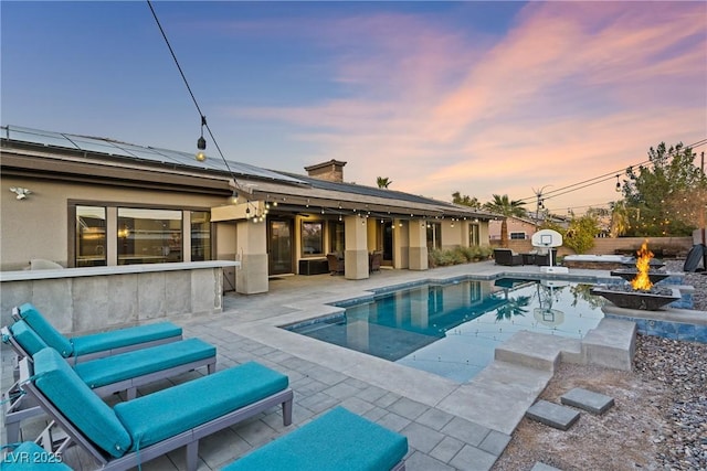 pool at dusk with a fire pit and a patio