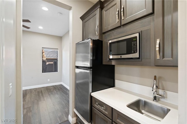 kitchen with ceiling fan, appliances with stainless steel finishes, dark wood-type flooring, dark brown cabinetry, and sink