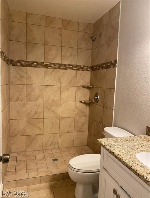 bathroom featuring toilet, vanity, a tile shower, and tile patterned flooring