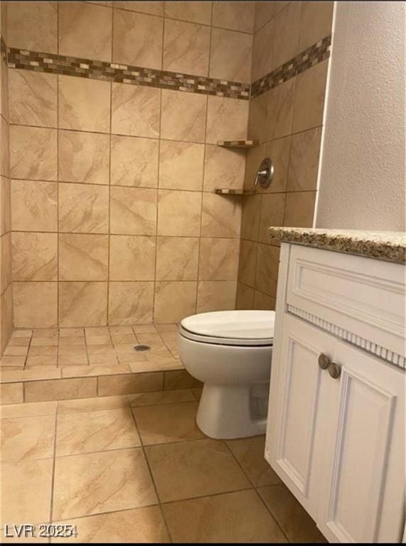 bathroom featuring toilet, vanity, tile patterned floors, and tiled shower