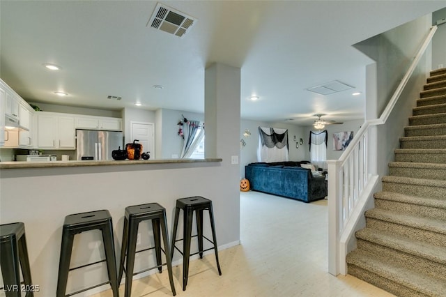 kitchen with white cabinets, a kitchen bar, stainless steel fridge with ice dispenser, kitchen peninsula, and ceiling fan