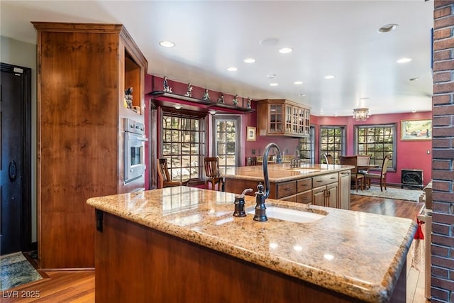 kitchen featuring sink, stainless steel oven, light stone counters, and a kitchen island with sink