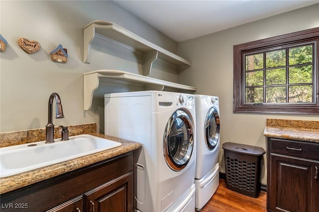 clothes washing area with cabinets, separate washer and dryer, wood-type flooring, and sink