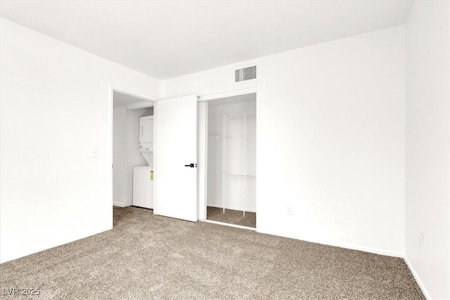 carpeted empty room with stacked washer and clothes dryer