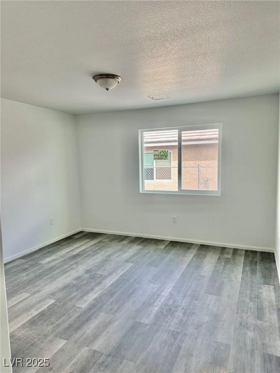 spare room featuring baseboards, a textured ceiling, and wood finished floors