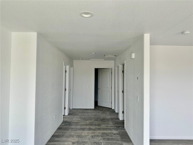 corridor featuring a textured ceiling, baseboards, and wood finished floors