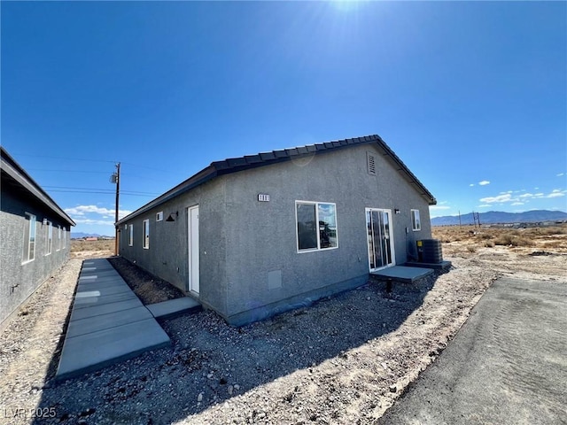view of side of property featuring central air condition unit, a mountain view, and stucco siding