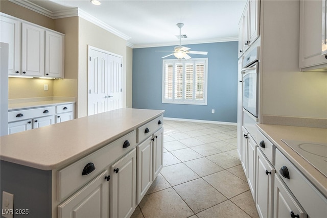 kitchen featuring white oven, light tile patterned floors, ceiling fan, ornamental molding, and white cabinets