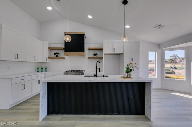 kitchen featuring sink, hanging light fixtures, white cabinets, and an island with sink