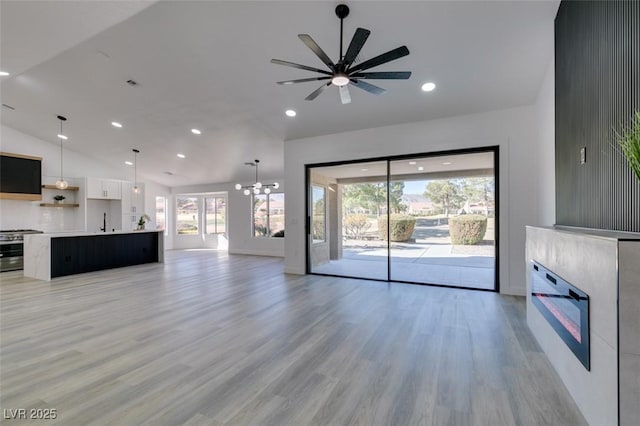 unfurnished living room featuring ceiling fan with notable chandelier, sink, vaulted ceiling, and light wood-type flooring