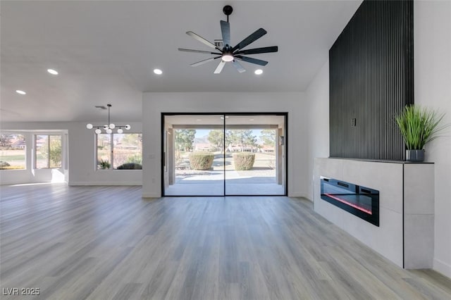 unfurnished living room featuring ceiling fan with notable chandelier and light hardwood / wood-style floors