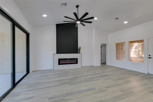 unfurnished living room with ceiling fan, light wood-type flooring, a large fireplace, and plenty of natural light