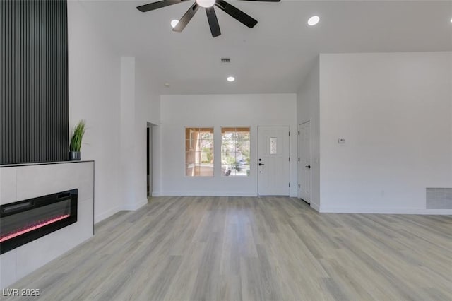 unfurnished living room featuring ceiling fan, a fireplace, and light wood-type flooring