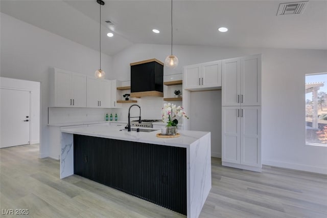 kitchen with hanging light fixtures, vaulted ceiling, an island with sink, and white cabinetry