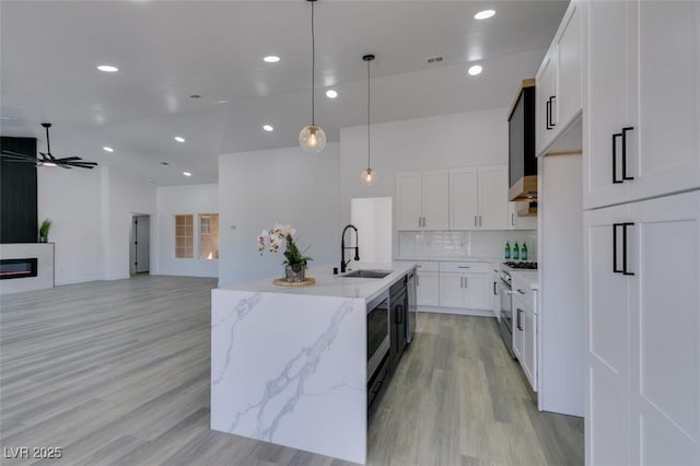 kitchen with white cabinets, an island with sink, sink, hanging light fixtures, and ceiling fan