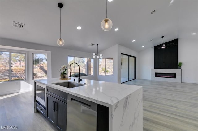 kitchen with light stone countertops, pendant lighting, appliances with stainless steel finishes, sink, and a kitchen island with sink