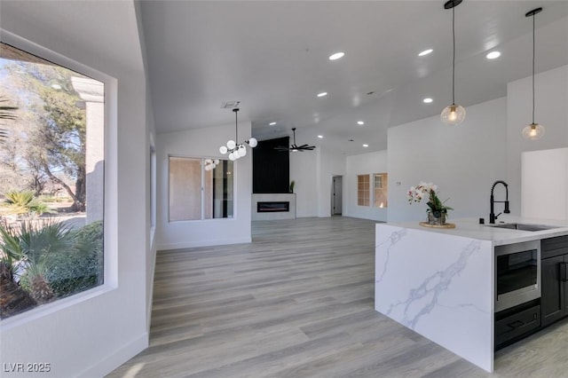 kitchen with ceiling fan, pendant lighting, sink, light stone countertops, and plenty of natural light