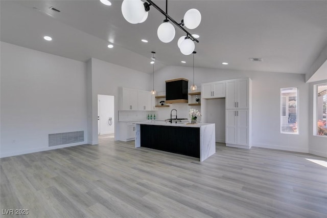 kitchen with white cabinets, decorative light fixtures, tasteful backsplash, sink, and a kitchen island with sink