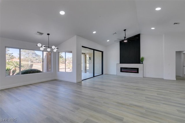 unfurnished living room with lofted ceiling, a large fireplace, ceiling fan with notable chandelier, and light hardwood / wood-style flooring