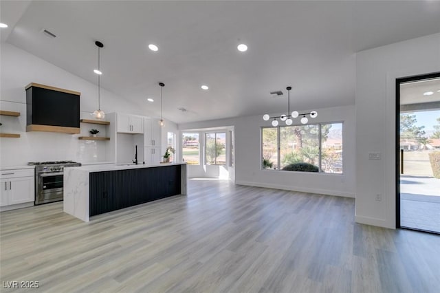 kitchen featuring white cabinetry, an island with sink, stainless steel stove, hanging light fixtures, and light wood-type flooring