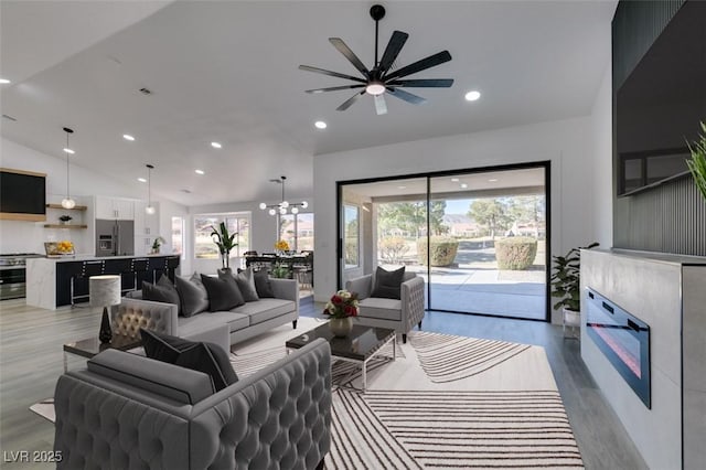 living room featuring lofted ceiling, ceiling fan with notable chandelier, and light hardwood / wood-style floors