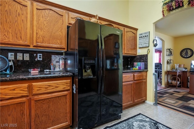 kitchen with light tile patterned flooring, black fridge, dark stone counters, and tasteful backsplash