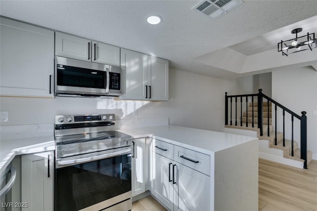 kitchen with light wood-type flooring, kitchen peninsula, stainless steel appliances, and a textured ceiling