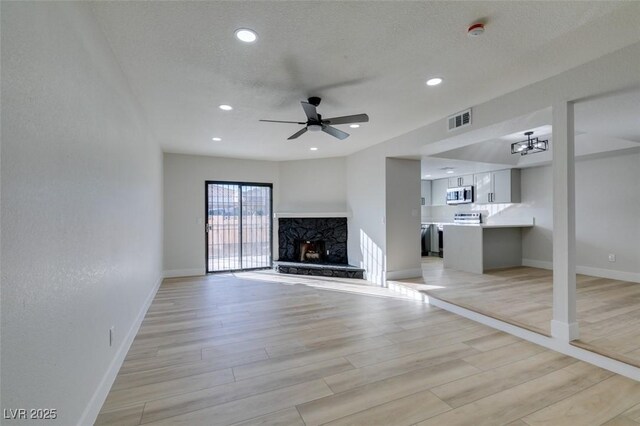 unfurnished living room featuring ceiling fan, a textured ceiling, light hardwood / wood-style flooring, and a premium fireplace