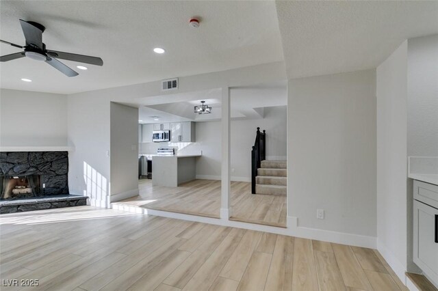 unfurnished living room with ceiling fan, light wood-type flooring, and a stone fireplace