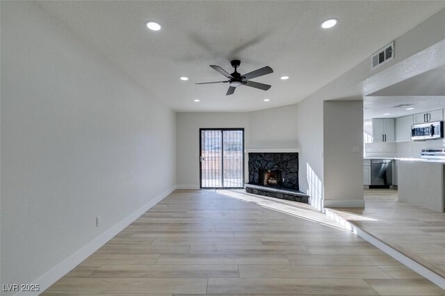 unfurnished living room with ceiling fan, a high end fireplace, and light wood-type flooring